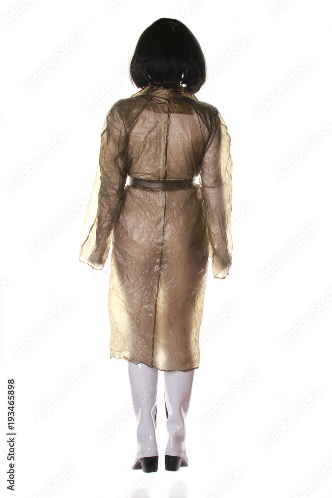 a truly strange old woman toying and posing in transparent retro raincoat  and rubber boots on white background isolated alone