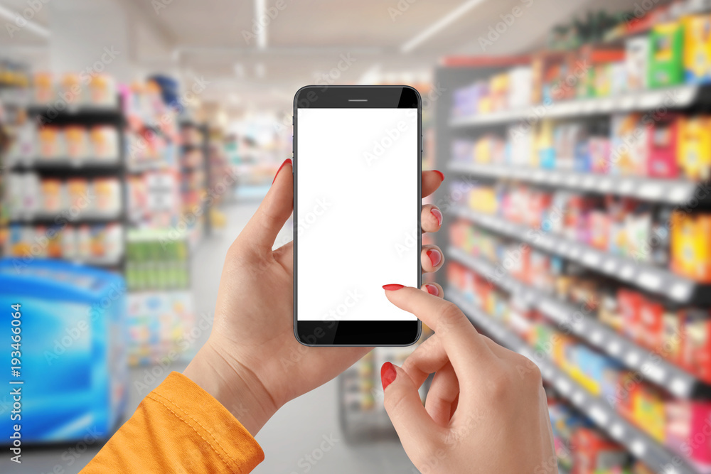 Woman use mobile phone with blank screen, blurred supermarket in background Woman use mobile phone with blank screen, blurred supermarket in background