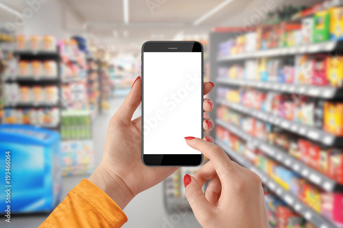 Woman use mobile phone with blank screen, blurred supermarket in background
