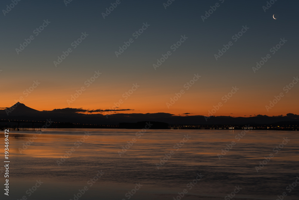 Small crescent moon and Venus over river and mountain at sunrise