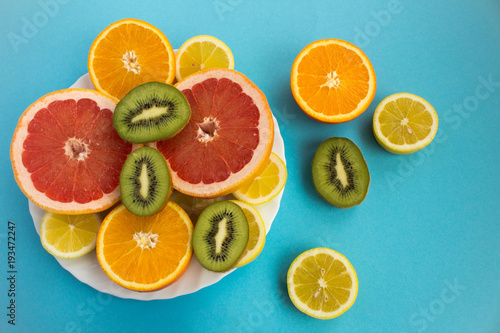 Sliced tropical fruits on the white plate on the blue background.Top view.