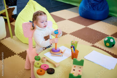 Little girl drawing with color pencils - sitting at the table with her toy bear