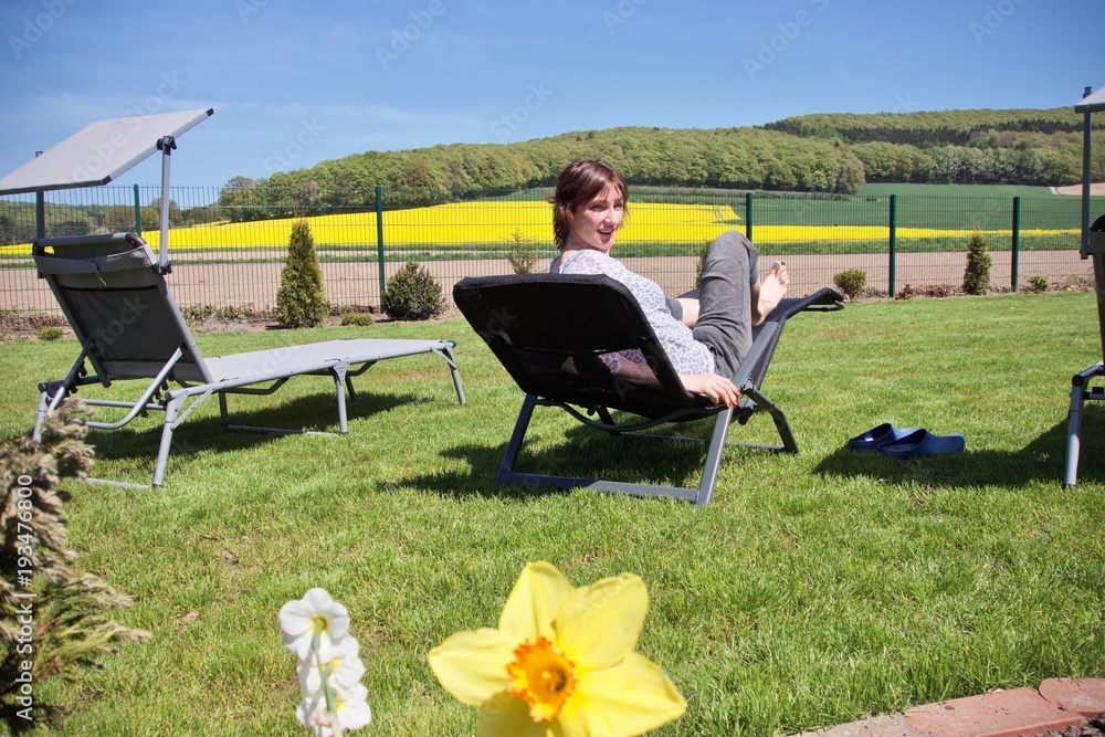 woman relaxing on a sun lounger with some hills and a rapeseed field in the background woman relaxing on a sun lounger with some hills and a rapeseed field in the background
