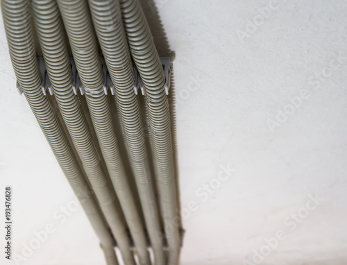 A close-up of several corrugated gray pipes are fixed to the ceiling with clips. Protective white PVC corrugated pipe channels w