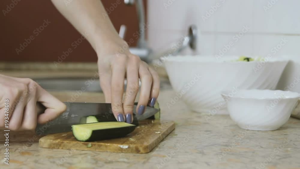 Close-up of woman hands cutting cucumber on cutting board in kitchen table. View side. Close-up of woman hands cutting cucumber on cutting board in kitchen table. View side.