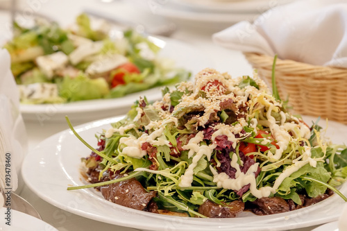 Salad from the mix of Italian herbs (iceberg, breeze, mung beans, arugula) and sun dried tomatoes on a white plate on a dark surface. Italian food. Vegetarian, vegan concept. photo