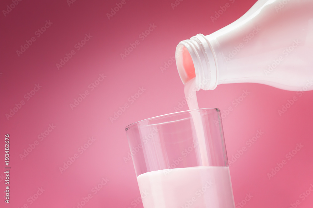 Pouring Yogurt From A White Bottle Into A Glass On A Pink Background