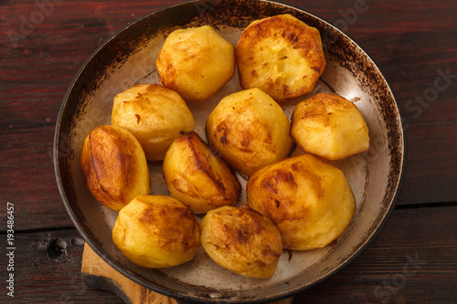 Savory golden roasted potato slices seasoned with fresh rosemary and bacon pieces and served in an old frying pan on a rustic wood table with copy space and a striped cloth