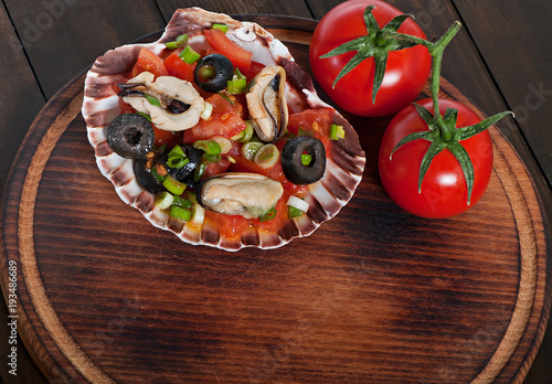 Salad of seafood mussels and vegetables tomato, decorated with green onions and olives.
