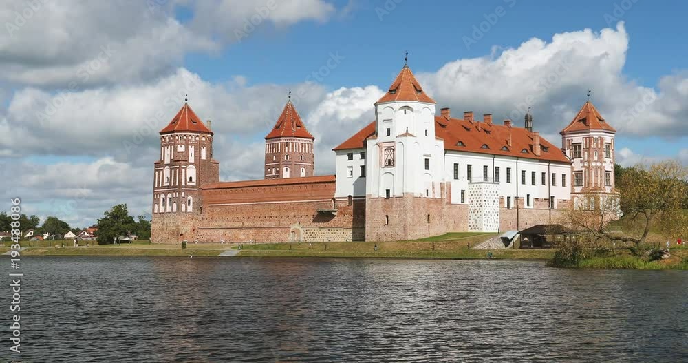 Mir, Belarus. Mir Castle Complex From Side Of Lake. Famous Landmark In Summer Sunny Day Under Blue Sky Mir, Belarus. Mir Castle Complex From Side Of Lake. Famous Landmark In Summer Sunny Day Under Blue Sky