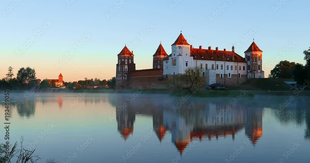 Mir, Belarus. Mir Castle Complex From Side Of Lake. Architectural Ensemble Of Feudalism, Ancient Cultural Monument. Famous Landmark. Misty Fog Above Lake In Summer Morning Mir, Belarus. Mir Castle Complex From Side Of Lake. Architectural Ensemble Of Feudalism, Ancient Cultural Monument. Famous Landmark. Misty Fog Above Lake In Summer Morning
