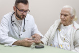 Lekarz Diabetolog trzyma palec wskazujący bardzo starej kobiety do nakłucia igłom w celu zbadania poziomu cukru we krwi.