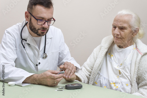 Lekarz Diabetolog trzyma palec wskazujący bardzo starej kobiety do nakłucia igłom w celu zbadania poziomu cukru we krwi.
