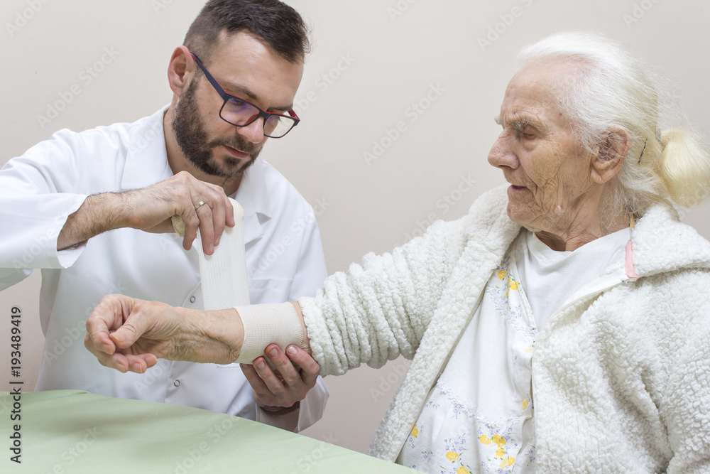 Lekarz zakłada opatrunek z bandaża na przedramię kobiety.  - obrazy, fototapety, plakaty 