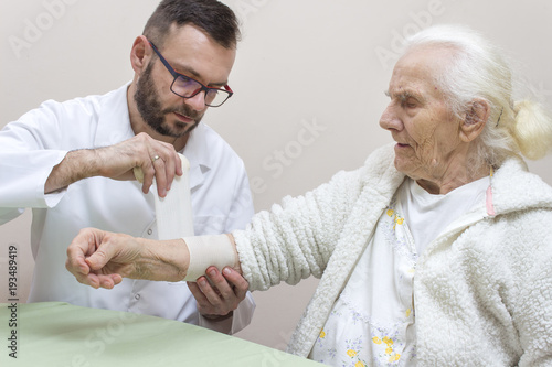 Lekarz zakłada opatrunek z bandaża na przedramię kobiety. 