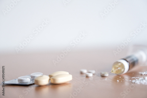 Heroin syringe needle wih heoin, cocaine powder and pills on the table.