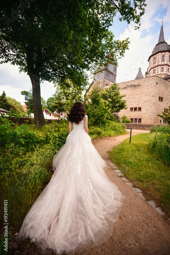 Wedding day. Gorgeous young beautiful bride in luxury tulle wedding dress with plume walking next to castle in France or Spain photo