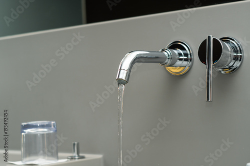 Luxury, design water tap with flowing water on silver wall. Selective focus.
