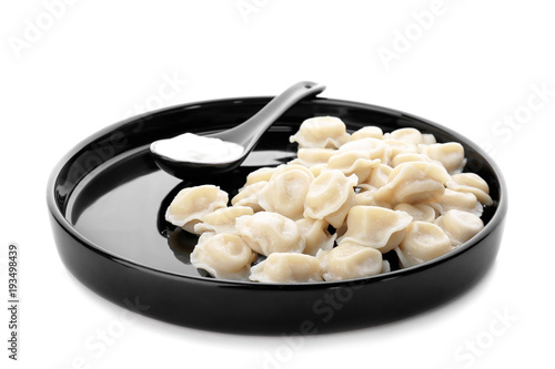Plate with tasty dumplings and sour cream on white background
