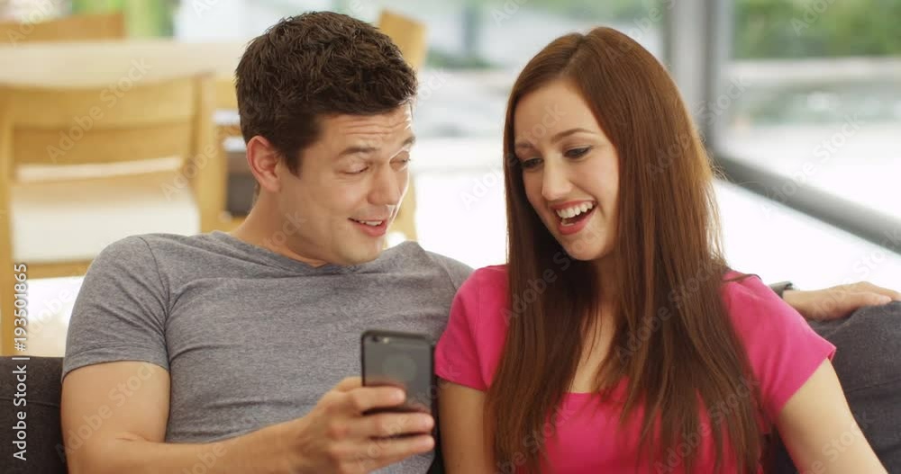 4K Cute young couple relaxing at home, talking & looking at smartphone. Slow motion 4K Cute young couple relaxing at home, talking & looking at smartphone. Slow motion
