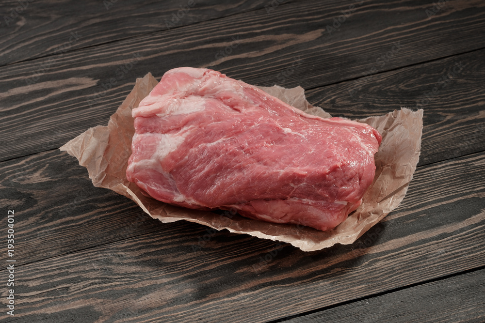 A piece of raw pork neck on paper. Pork tenderloin on paper on a dark background A piece of raw pork neck on paper. Pork tenderloin on paper on a dark background