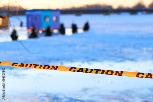 Caution sign of thin ice in the fishing village installed on the lake at risk of drowning. Warning or caution sign of drowning, frozen lake formed by a dam in the winter.