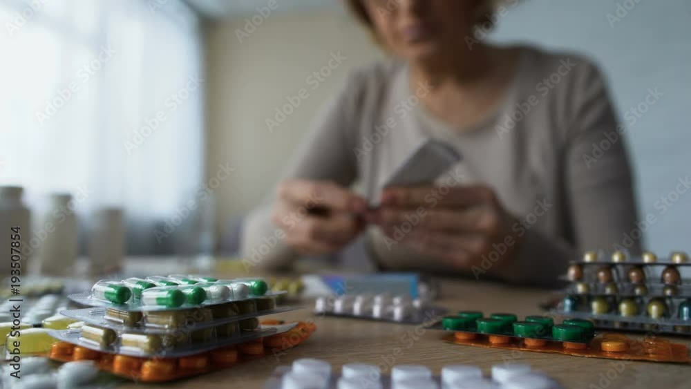 Closeup view of pills on table and old woman taking medicine behind, consumerism Closeup view of pills on table and old woman taking medicine behind, consumerism