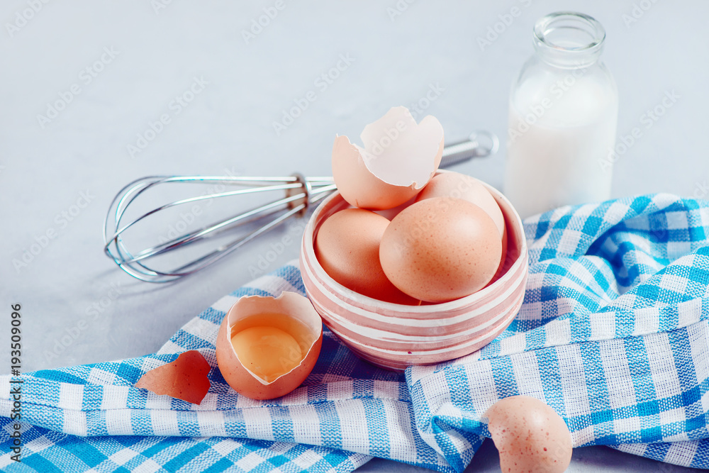 Brown eggs in a ceramic bowl on a light background with milk, flour and ingredients for Easter cooking. High key background with copy space. Brown eggs in a ceramic bowl on a light background with milk, flour and ingredients for Easter cooking. High key background with copy space.