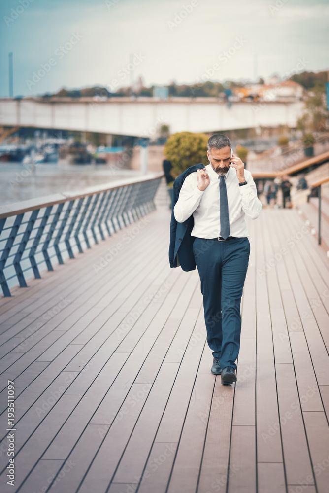 Casual senior business man walking the street and talking on his cell phone, urban outdoor area