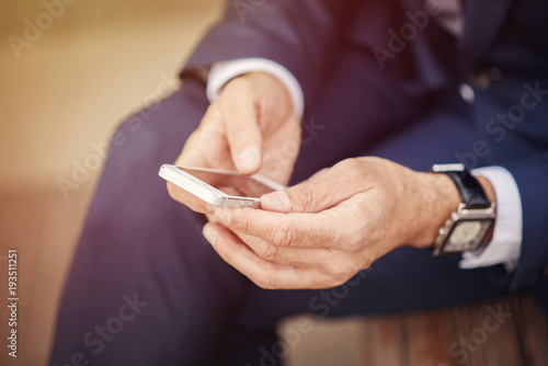 Senior business man typing a text message on his cellphone  sitting on a bench in a park closeup