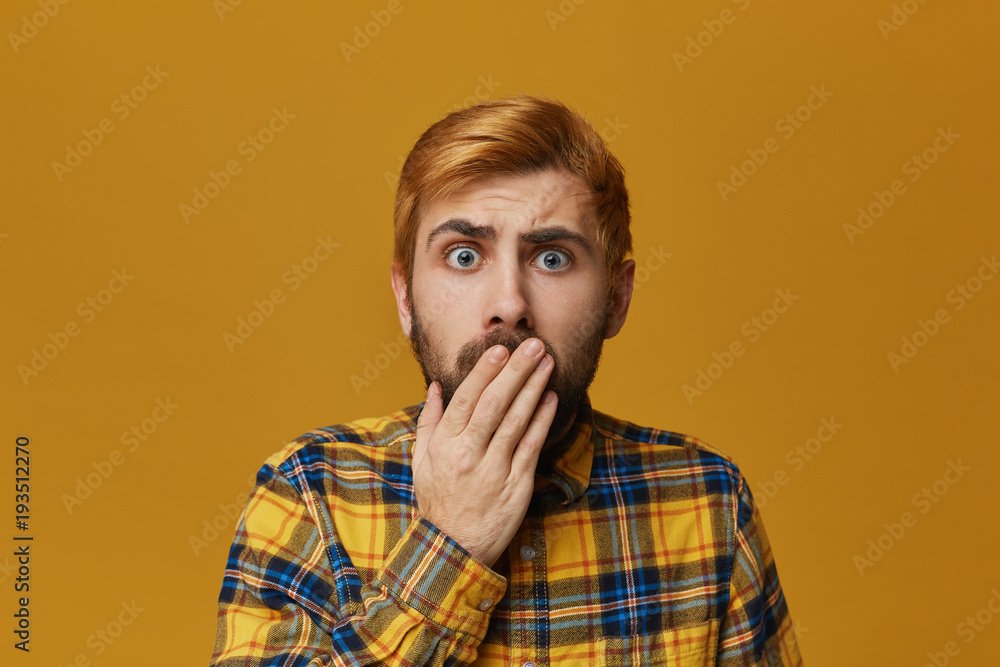 Amazed and astonished male wears checkered yellow shirt with beard and dyed red hair bieng shocked. Isolated over yellow background. Facial Expression Amazed and astonished male wears checkered yellow shirt with beard and dyed red hair bieng shocked. Isolated over yellow background. Facial Expression