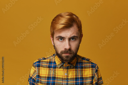 Portrait of young hipster male with dyed redhead and beard bieng mad and angry about some problems. Facial expression. Isolated over yellow background. © timtimphoto