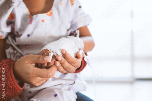 Mother hand holding sick daughter hand who have IV solution bandaged in the hospital with love and care