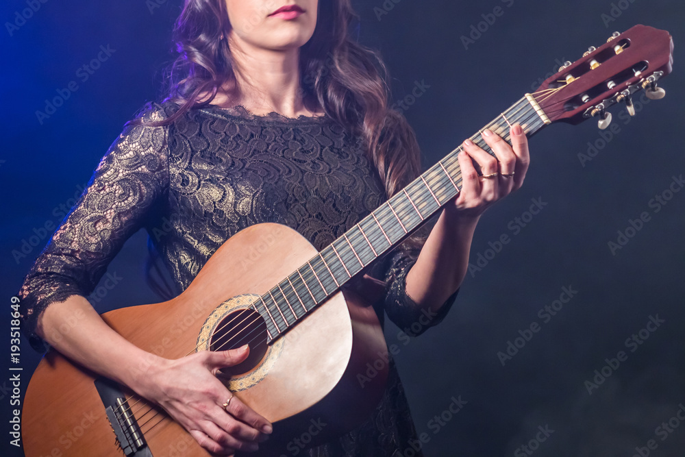 Obraz premium Acoustic guitar in the hands of a girl with long dark hair. Smoky blue background.