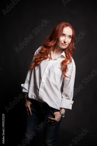 Portrait of a beautiful girl with long red hair in a white man's shirt on a dark background in the studio