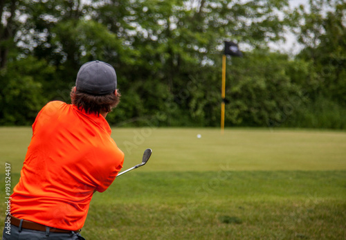 Golfer chipping his ball onto the green right at the pin