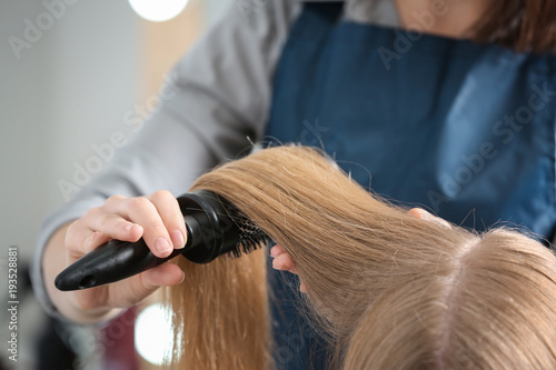 Professional hairdresser brushing client's hair in beauty salon