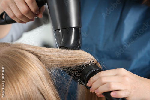 Professional hairdresser drying client's hair in beauty salon