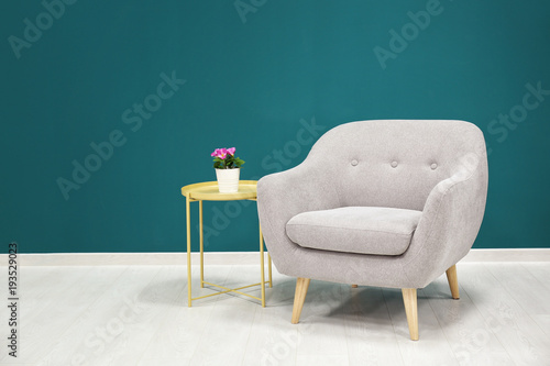 Trendy armchair with table near shaded spruce wall