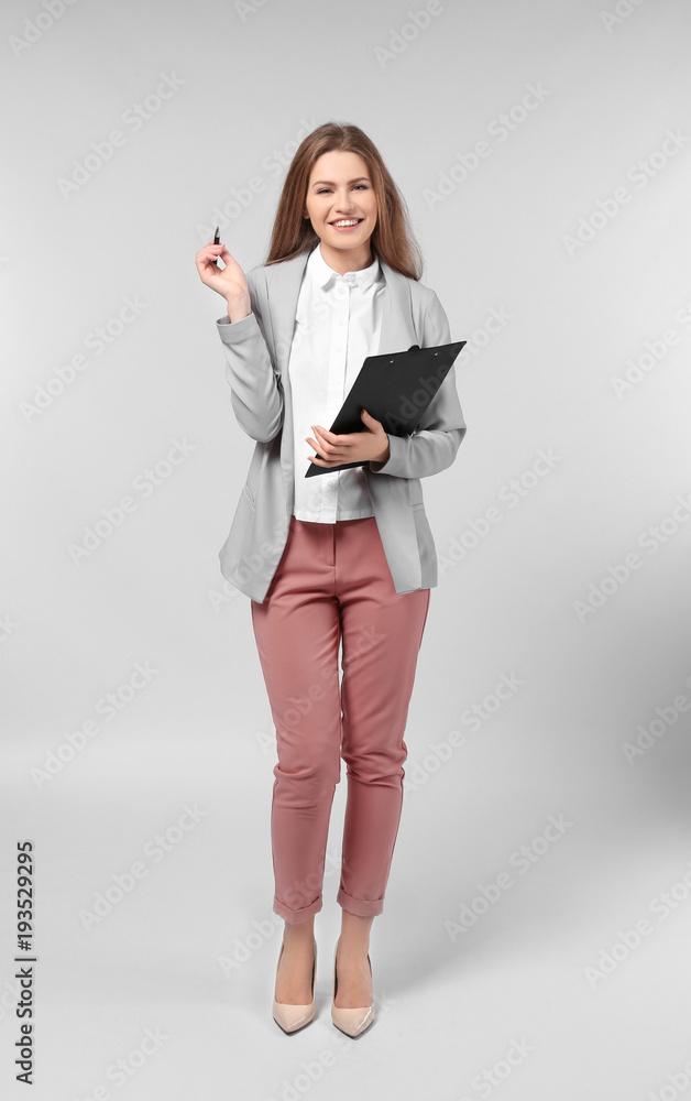 Fototapeta premium Beautiful young woman in elegant suit and with clipboard on light background