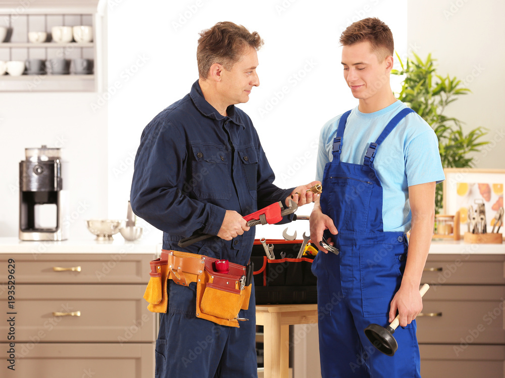 Plumber with young trainee on kitchen Plumber with young trainee on kitchen