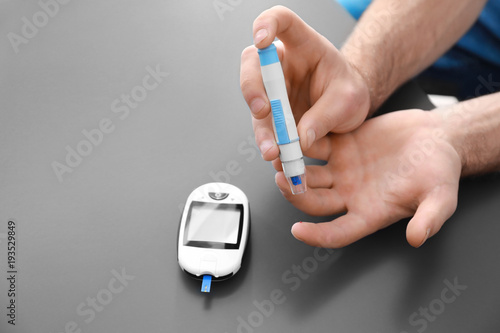 Diabetic man using lancet pen and digital glucometer on grey background