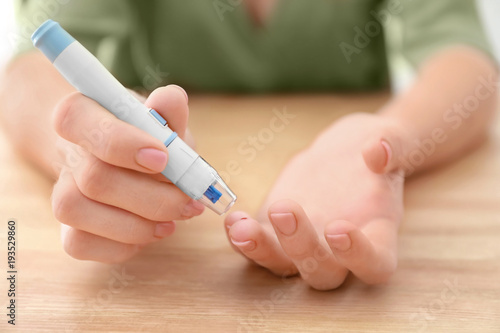 Diabetic woman taking blood sample with lancet pen at wooden table  closeup