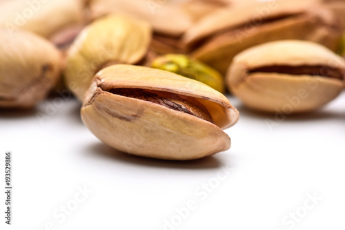 Roasted pistachio nut (Pistacia vera) seed in shell with more nuts in background and white foreground