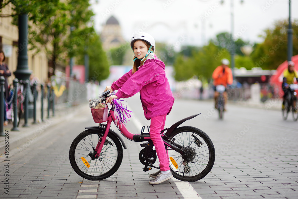 Fototapeta premium Cute little girl riding a bike in a city wearing helmet on summer day