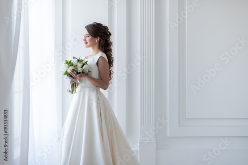 attractive happy bride posing in traditional dress with wedding bouquet