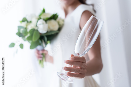 selective focus of bride with wedding bouquet holding empty champagne glass
