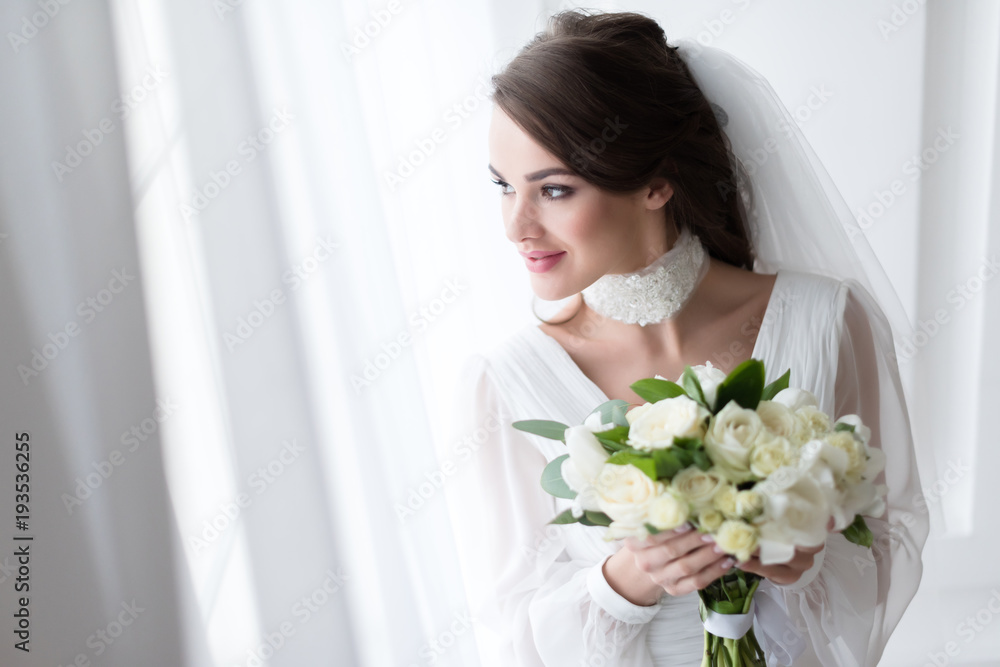 smiling bride in wedding dress and veil holding white bouquet smiling bride in wedding dress and veil holding white bouquet