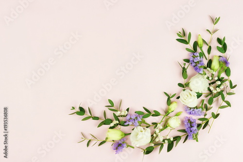 Flowers background. Frame wreath of green eucalyptus branches and white and purple flowers on pale pink background. top view. copy space. Holidays background