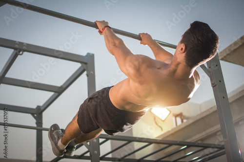 Handsome muscular man doing exercises on horizontal bar outdoors. Calisthenics workout.